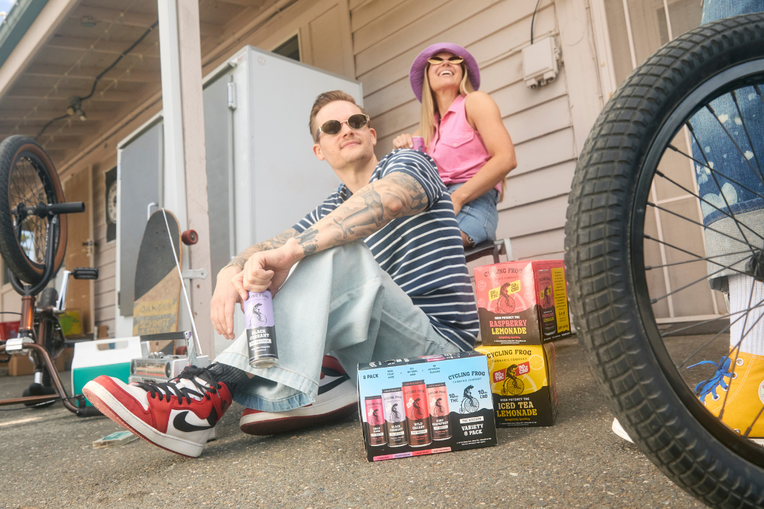 Man and woman sitting on the ground next to 5mg, 10mg, and 50mg Cycling Frog beverages